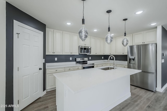 kitchen with pendant lighting, sink, appliances with stainless steel finishes, a kitchen island with sink, and light wood-type flooring