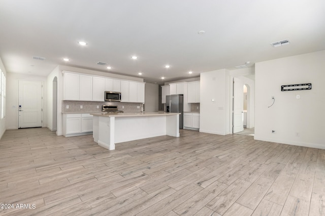 kitchen with appliances with stainless steel finishes, an island with sink, white cabinetry, decorative backsplash, and light hardwood / wood-style flooring