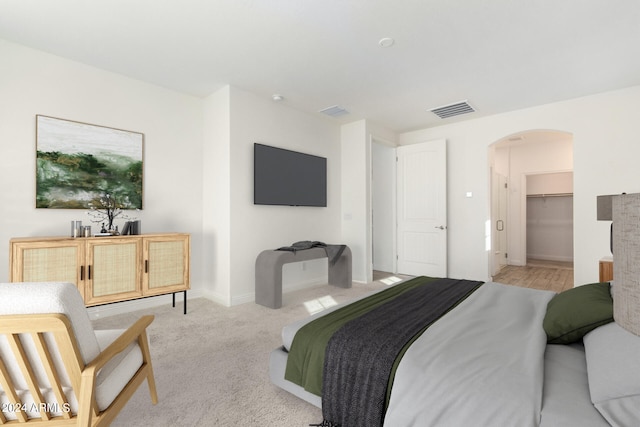 bedroom with a walk in closet, a closet, and light colored carpet