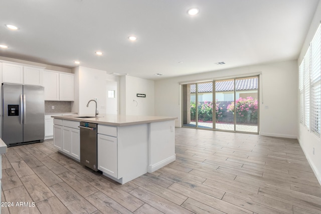 kitchen with white cabinets, stainless steel appliances, a center island with sink, and sink