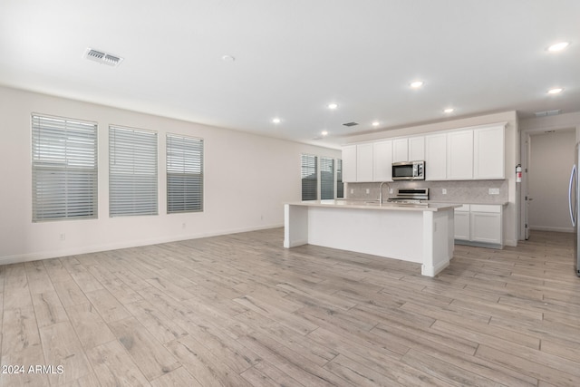 kitchen with white cabinets, a center island with sink, light wood-type flooring, a wealth of natural light, and stainless steel appliances