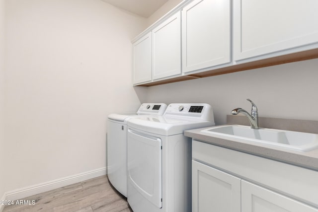 clothes washing area featuring light hardwood / wood-style floors, washer and dryer, sink, and cabinets