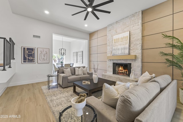 living area with ceiling fan, a fireplace, visible vents, baseboards, and light wood-style floors