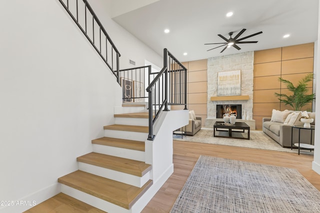 stairway featuring baseboards, a ceiling fan, wood finished floors, a stone fireplace, and recessed lighting