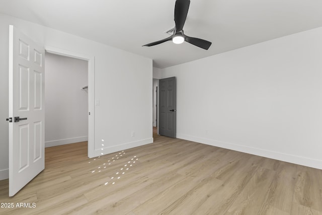 unfurnished bedroom with ceiling fan, a spacious closet, light wood-type flooring, and baseboards