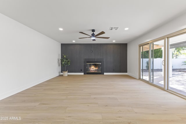 unfurnished living room featuring recessed lighting, visible vents, light wood-style floors, a glass covered fireplace, and an accent wall