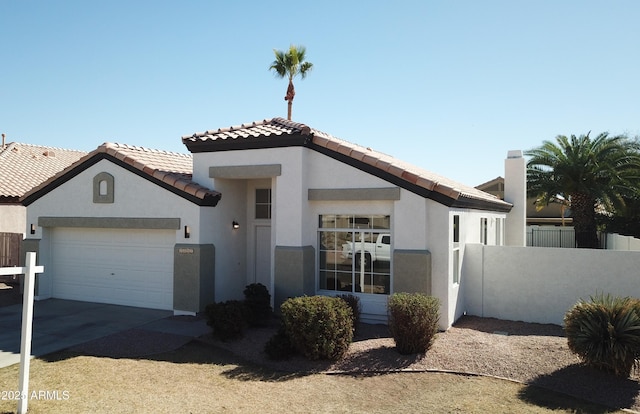 mediterranean / spanish-style home featuring a tile roof, stucco siding, concrete driveway, an attached garage, and fence