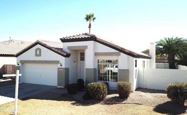 mediterranean / spanish home with an attached garage, fence, concrete driveway, a tiled roof, and stucco siding