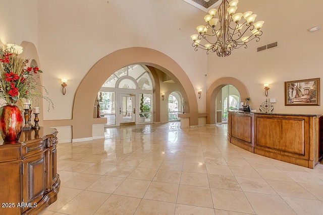 foyer entrance with arched walkways, a high ceiling, visible vents, baseboards, and an inviting chandelier