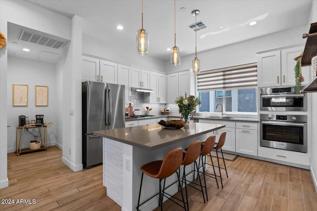 kitchen with pendant lighting, appliances with stainless steel finishes, light hardwood / wood-style flooring, and white cabinetry