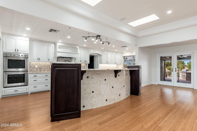 kitchen featuring decorative backsplash, a kitchen breakfast bar, a skylight, double oven, and white cabinetry