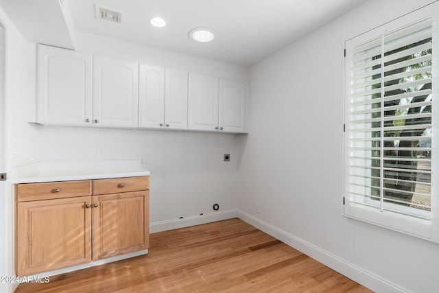 clothes washing area featuring cabinets, light hardwood / wood-style flooring, and electric dryer hookup