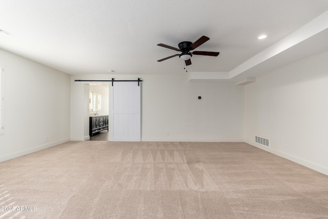 unfurnished room with a barn door, light carpet, and ceiling fan