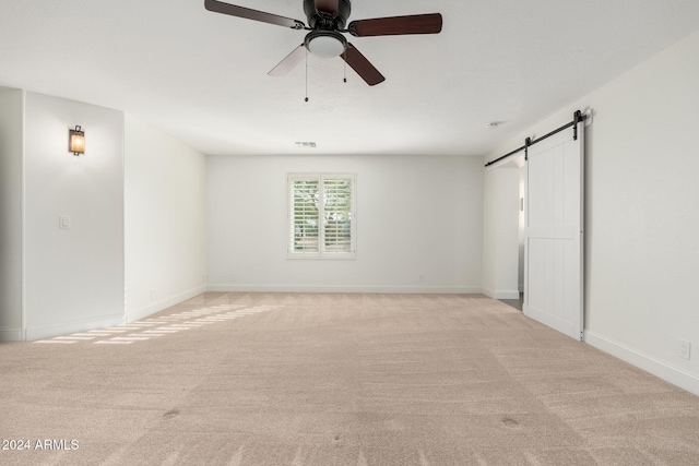 unfurnished room featuring ceiling fan, a barn door, and light colored carpet