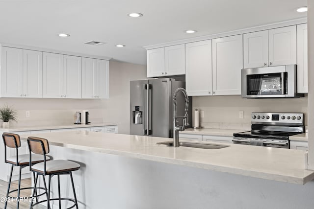 kitchen featuring white cabinetry, sink, stainless steel appliances, a breakfast bar area, and a center island with sink