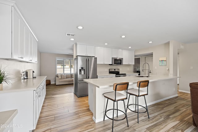 kitchen with stainless steel appliances, sink, a center island with sink, light hardwood / wood-style flooring, and white cabinets