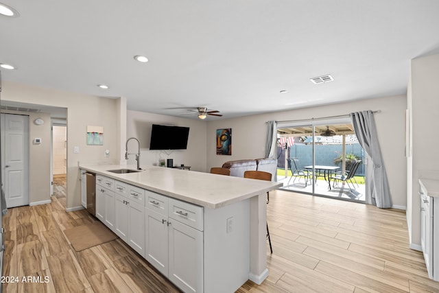 kitchen featuring kitchen peninsula, ceiling fan, sink, white cabinets, and a breakfast bar area