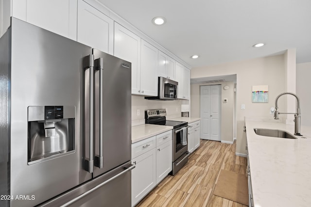 kitchen with white cabinets, sink, light stone countertops, light wood-type flooring, and stainless steel appliances