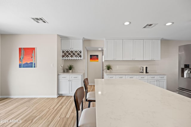 kitchen featuring white cabinets, stainless steel refrigerator with ice dispenser, light hardwood / wood-style floors, and light stone countertops