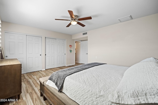 bedroom featuring ceiling fan, light hardwood / wood-style floors, and two closets