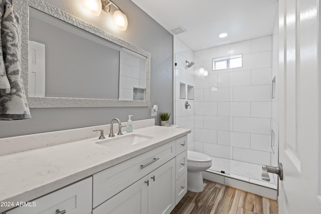 bathroom featuring a tile shower, vanity, hardwood / wood-style flooring, and toilet