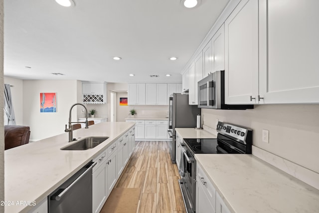 kitchen with white cabinetry, sink, stainless steel appliances, light stone counters, and light hardwood / wood-style flooring