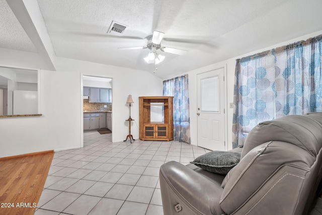 living room with ceiling fan, light tile patterned floors, and a textured ceiling