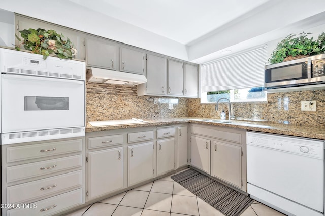 kitchen featuring gray cabinetry, white appliances, sink, light tile patterned floors, and tasteful backsplash