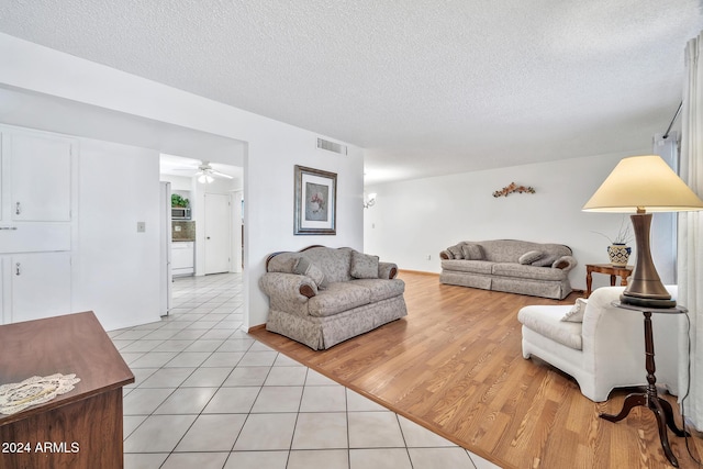 living room with a textured ceiling, light wood-type flooring, and ceiling fan