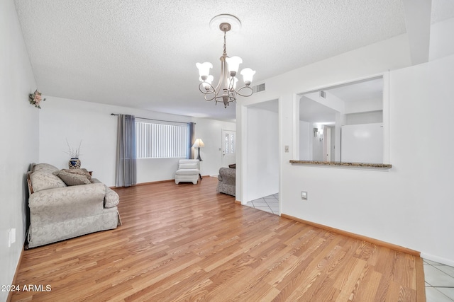 living room with light wood-type flooring, a textured ceiling, and an inviting chandelier