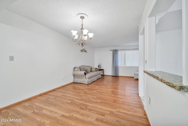 unfurnished room with a textured ceiling, a notable chandelier, and light wood-type flooring