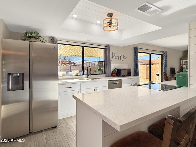 kitchen with a raised ceiling, sink, white cabinets, and black appliances