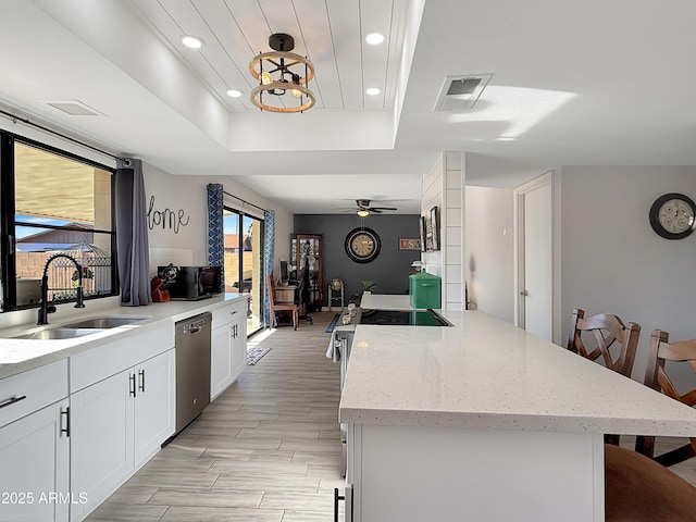 kitchen featuring white cabinetry, sink, a center island, stainless steel dishwasher, and a tray ceiling