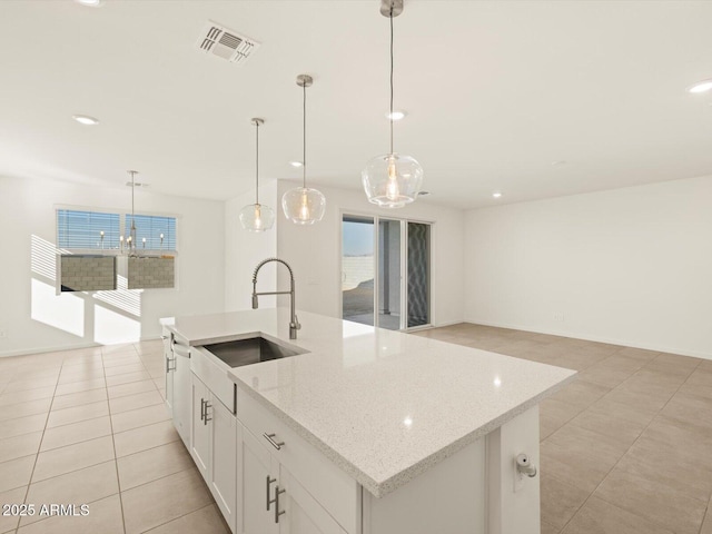 kitchen featuring pendant lighting, white cabinetry, sink, a kitchen island with sink, and light stone counters