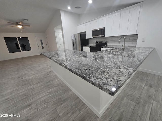 kitchen featuring stone counters, kitchen peninsula, decorative backsplash, white cabinetry, and appliances with stainless steel finishes