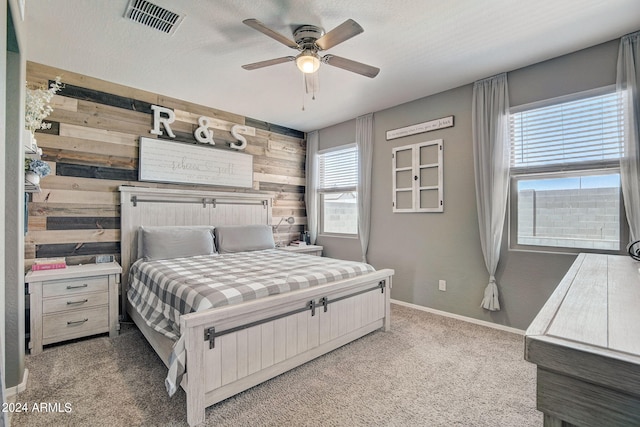 bedroom with wooden walls, a ceiling fan, visible vents, baseboards, and light colored carpet