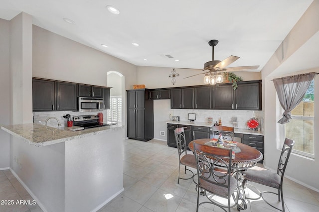 kitchen with light stone counters, vaulted ceiling, appliances with stainless steel finishes, kitchen peninsula, and decorative backsplash