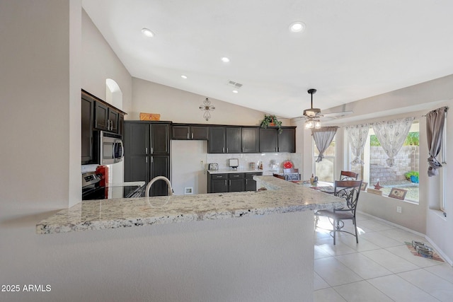 kitchen with lofted ceiling, dark brown cabinets, appliances with stainless steel finishes, kitchen peninsula, and light stone countertops