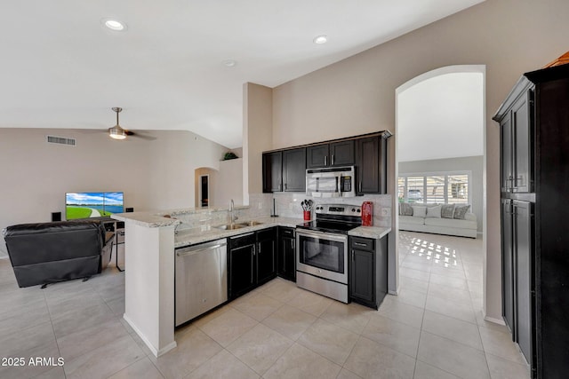 kitchen with sink, stainless steel appliances, light stone countertops, decorative backsplash, and kitchen peninsula