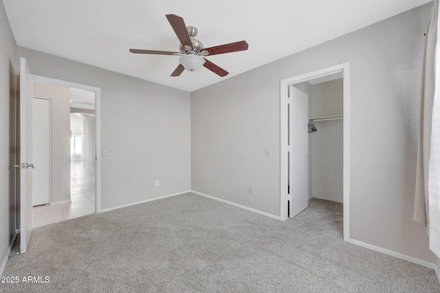 unfurnished bedroom featuring a walk in closet, light colored carpet, ceiling fan, and a closet