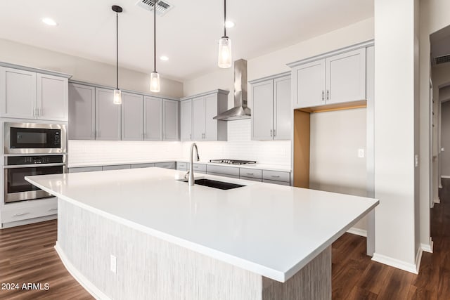 kitchen featuring a center island with sink, stainless steel appliances, wall chimney exhaust hood, and sink