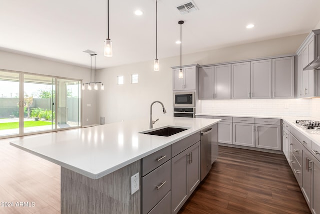 kitchen featuring sink, decorative light fixtures, a center island with sink, dark wood-type flooring, and stainless steel appliances