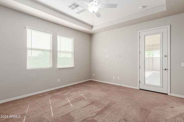 unfurnished room with ceiling fan, light colored carpet, a raised ceiling, and a wealth of natural light