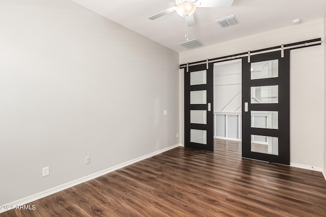 unfurnished room with a barn door, ceiling fan, and dark wood-type flooring