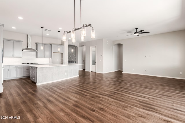 kitchen featuring hanging light fixtures, dark hardwood / wood-style flooring, wall chimney range hood, and an island with sink