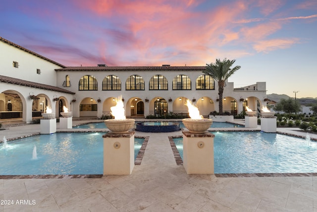 pool at dusk with pool water feature and a patio