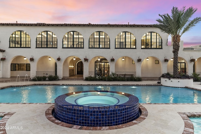 pool at dusk featuring an in ground hot tub, pool water feature, and a patio