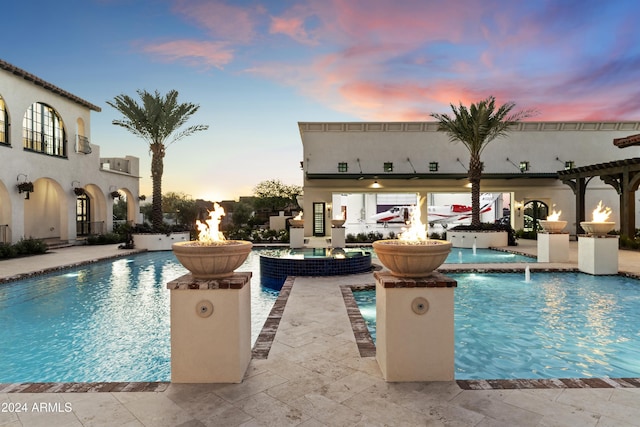 pool at dusk featuring pool water feature and a patio