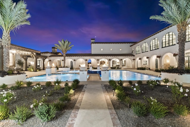 pool at dusk featuring pool water feature and a patio area