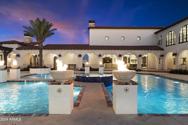 pool at dusk with an in ground hot tub and a patio